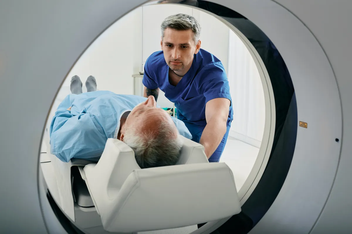 A radiographer helping a patient lie on the bed of a CT scanner