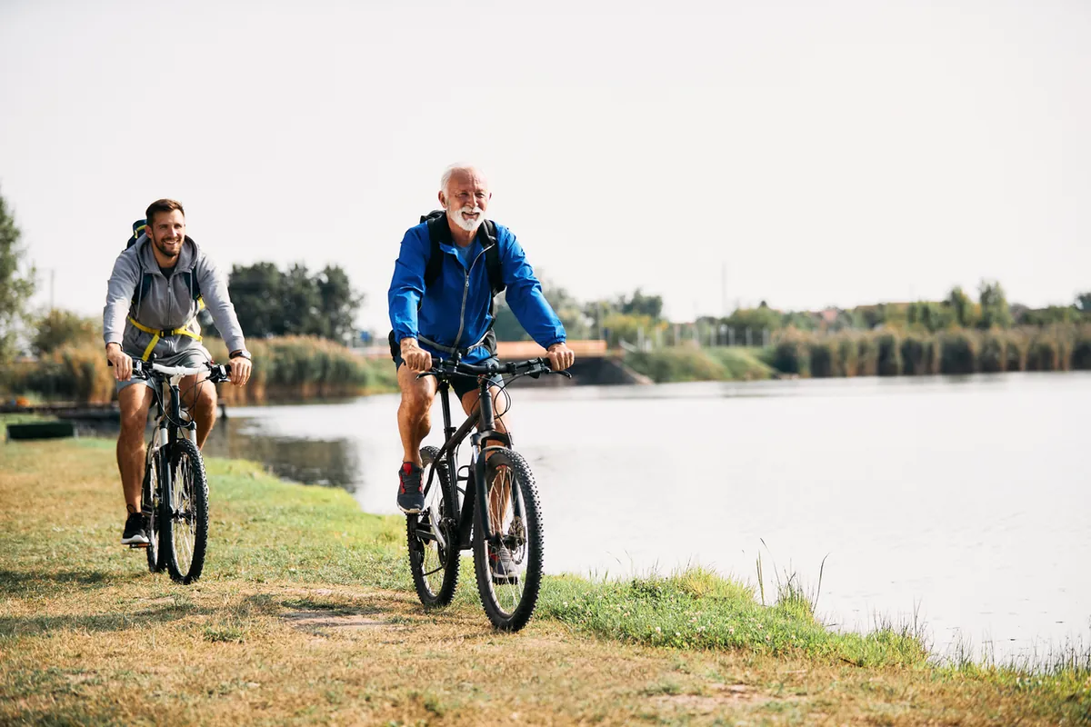 Two men cycling along a grassy riverside path