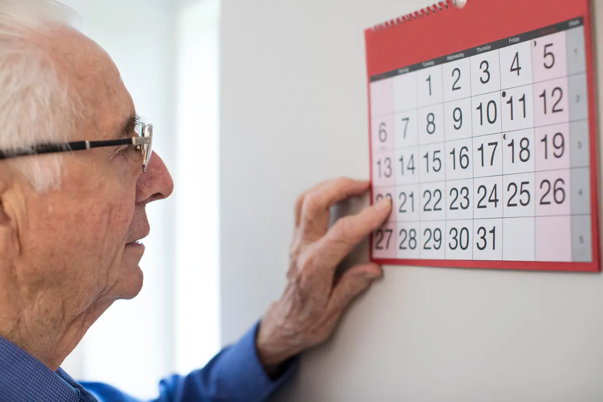 An older man in glasses pointing to a date on a wall calendar