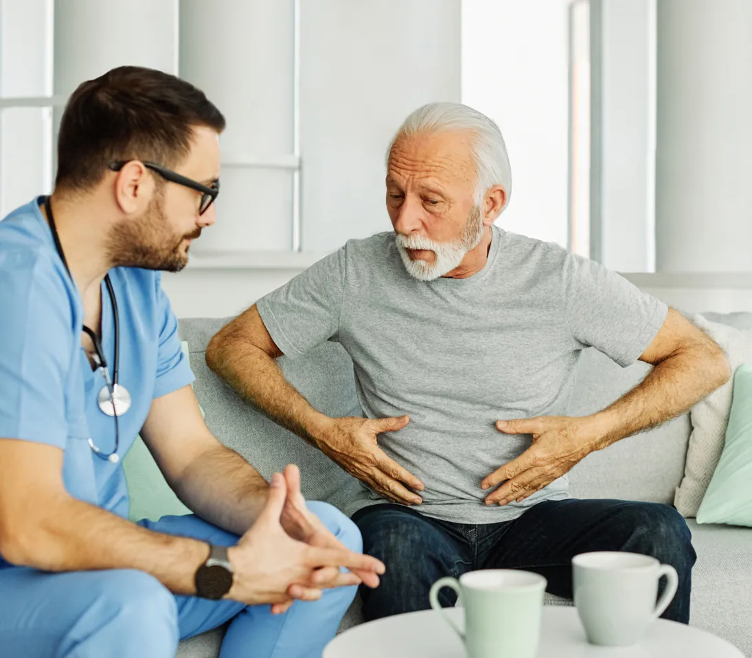 An older man describing pain in his abdomen to a clinician in blue scrubs
