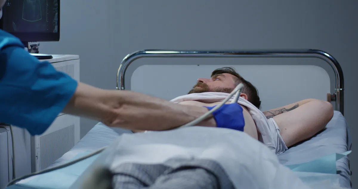 Close-up of an ultrasound probe being moved over a man's upper abdomen