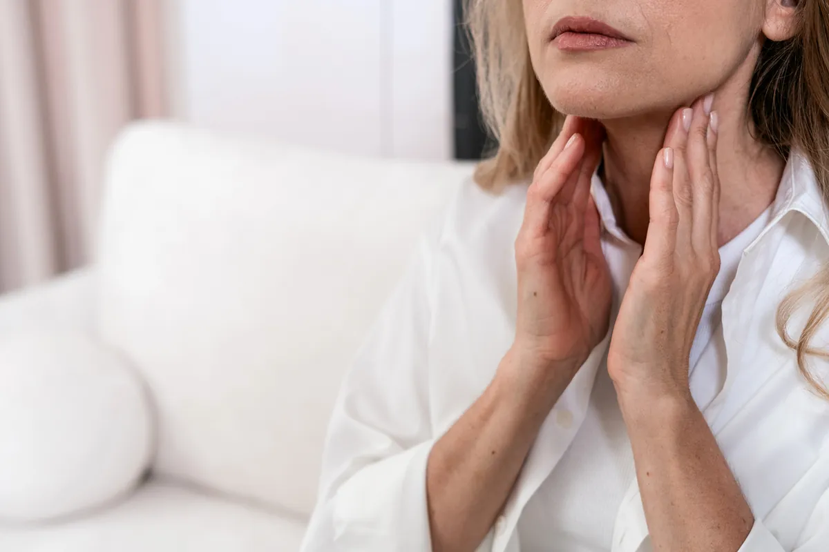 A woman touching the front of her neck, where the thyroid gland sits