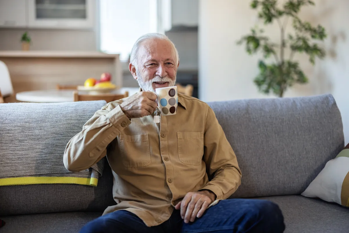 A smiling older man relaxing on a sofa at home with a mug of tea