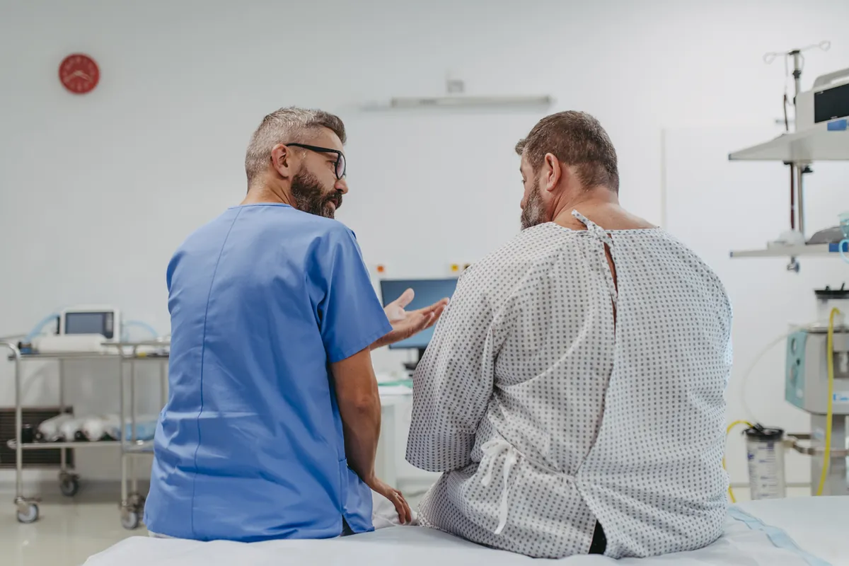 A surgeon in blue scrubs talking with a patient in a hospital gown before an operation