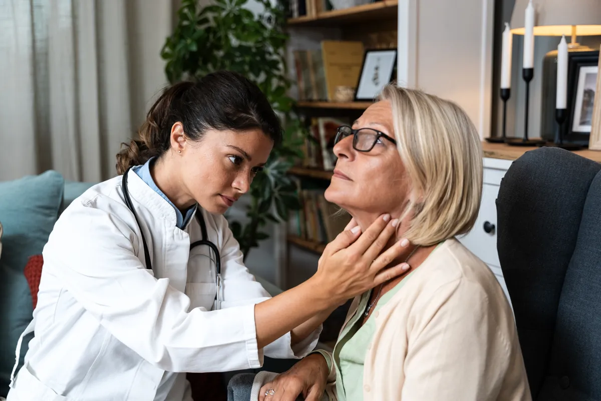 A doctor gently feeling the front of a woman's neck to examine her thyroid gland