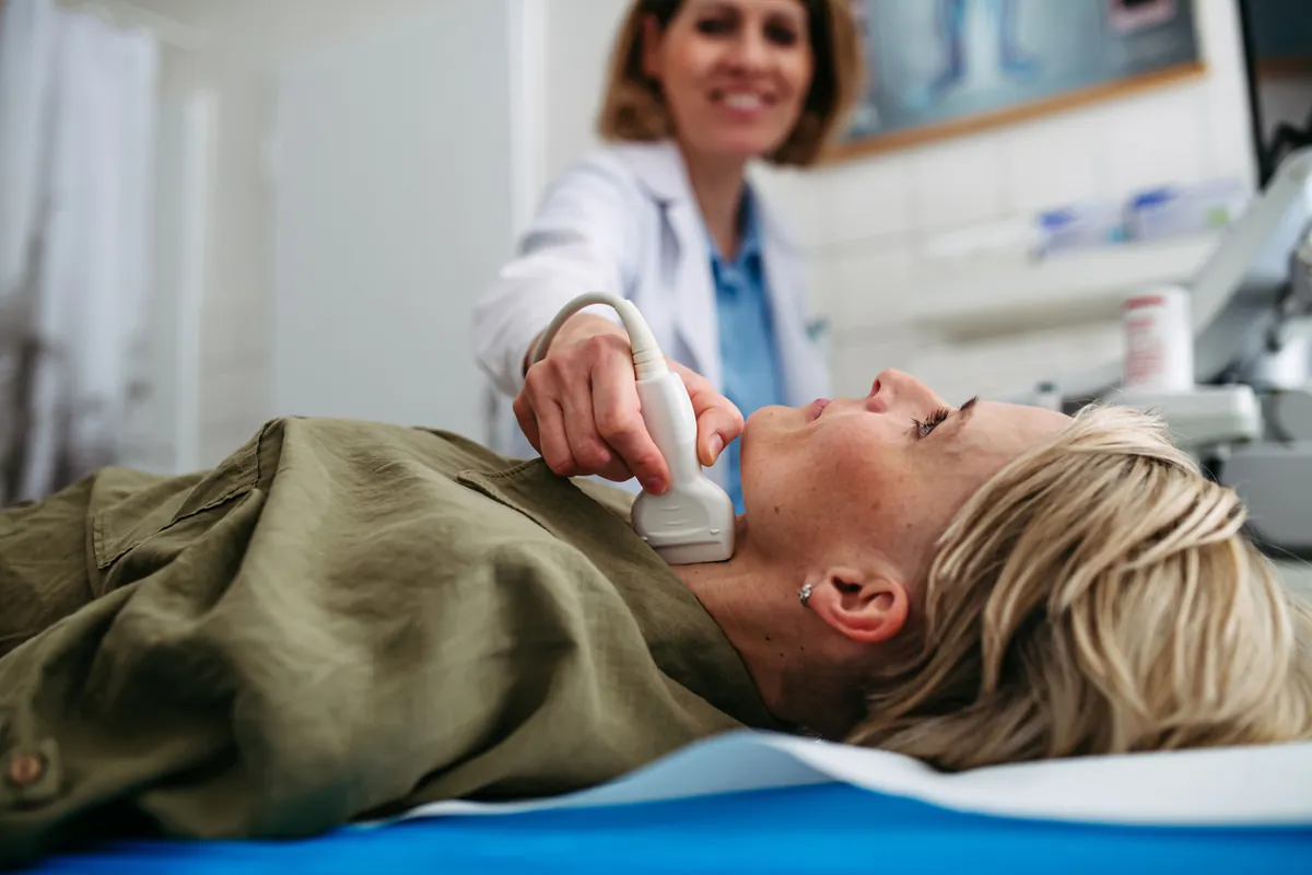 A clinician scanning the front of a woman's neck with an ultrasound probe