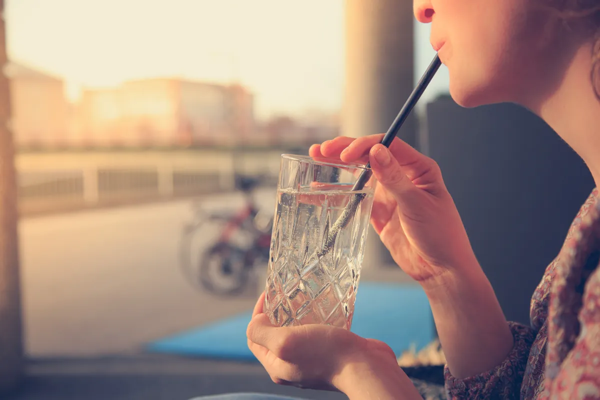 A woman holding a glass of water with a straw to her lips